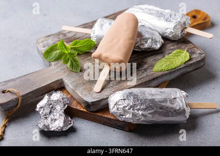 Gelato artigianale in glassa al cioccolato su una tavola da portata in legno, messa a fuoco selettiva. Sfondo grigio texture Foto Stock