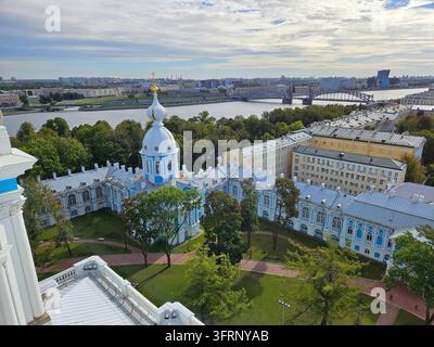 Il grande edificio della cattedrale di Smolny con una cupola blu si trova di fronte a un parco verde. L'edificio è circondato da alberi e ha un grande cortile davanti Foto Stock