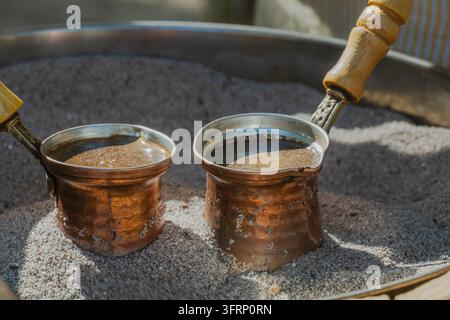 Prima vista di due cezve di rame che preparano il caffè turco tradizionale nella sabbia calda, con una ricca schiuma che si forma in superficie durante la lenta preparazione tradizionale Foto Stock