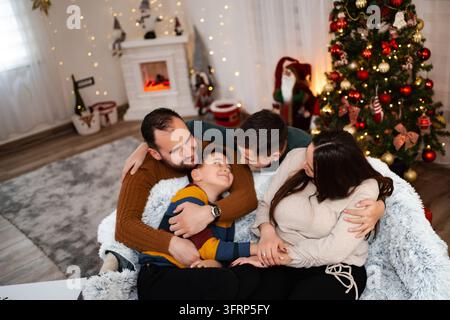 Famiglia che si abbraccia e celebra le festività natalizie a casa Foto Stock