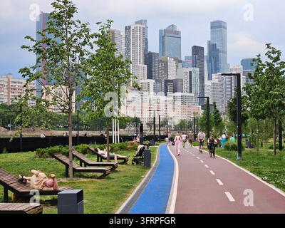 MOSCA - 5 GIUGNO 2024: Un gruppo di persone cammina su un sentiero in un parco. Ci sono panchine e una pista ciclabile. argini e grattacieli a Mosca, in Russia Foto Stock