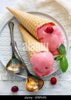 Gelato ai mirtilli in coni di waffle su un piatto bianco e cucchiai da dessert, messa a fuoco selettiva Foto Stock