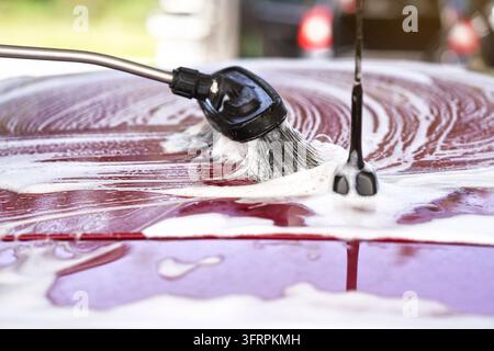 Spazzola lasciando i colpi in shampoo bianco e schiuma sul tetto di auto rossa lavata in autolavaggio Foto Stock