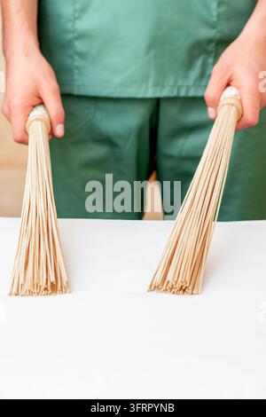 Prima di mani di un massaggiatore che tiene scope da massaggio in bambù sul tavolo Foto Stock