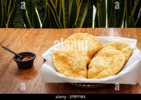 Empanadas cilene dorate servite in un cestino con un contorno di salsa al pepe aji piccante su un tavolo di legno Foto Stock