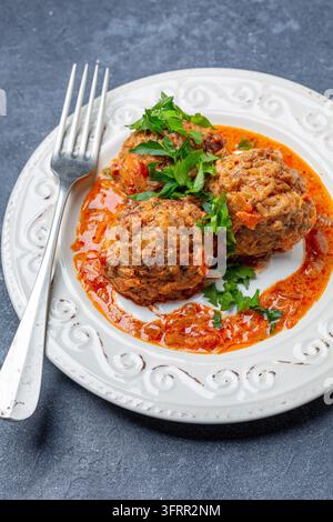 Polpette fatte in casa con salsa al pomodoro e panna acida in un piatto su uno sfondo scuro e strutturato Foto Stock
