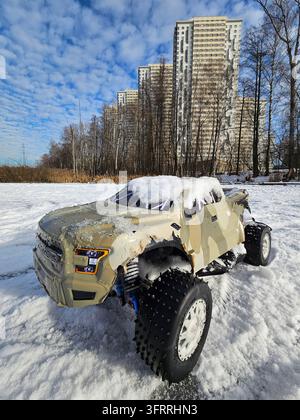 Un camion giocattolo coperto di neve si trova su un campo innevato. Il camion è mimetizzato ed è un veicolo militare. Il paesaggio innevato e la mimetizzazione del camion suggeriscono un senso di avventura ed esplorazione Foto Stock