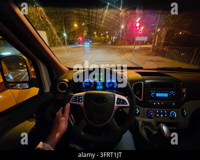 Una persona guida un furgone camion e il volante è al centro dell'auto. L'auto è su una strada con un semaforo rosso Foto Stock