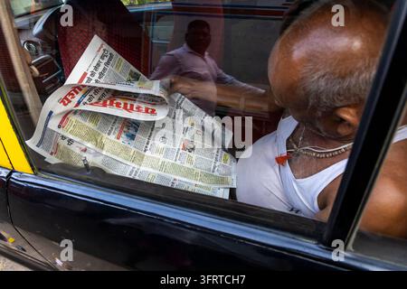 Uomo anziano che legge un giornale in lingua hindi all'interno di un taxi nero e giallo con il riflesso di un altro uomo nel finestrino dell'auto, Maharashtra, Mumbai, India Foto Stock