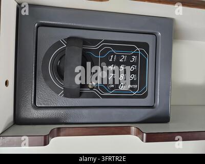 La cassaforte digitale si trova ordinatamente all'interno di un mobile in legno. Tastierino nero con numeri e una maniglia. Design moderno, sicuro e compatto. Si adatta bene ai piccoli spazi di stoccaggio. Pulito, funzionale e pratico Foto Stock