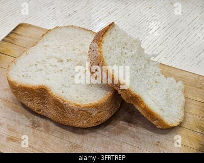 Fetta di pane appena sfornato poggia su tavola di legno. L'interno morbido contrasta con la crosta dorata e rustica. Una consistenza friabile invita a un gusto caldo e fatto in casa. Esposizione semplice e appetitosa perfetta per i contenuti alimentari Foto Stock
