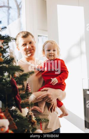 Padre che tiene il figlio neonato vicino all'albero di Natale a casa Foto Stock