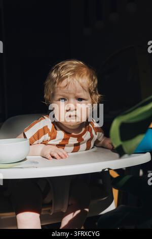 Bambino che fa una faccia buffa mentre prova il cibo nella sedia alta Foto Stock