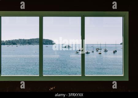Ho scattato questa foto alla stazione ferroviaria di Villefranche attraverso la finestra che si affaccia sulla baia con barche ormeggiate in lontananza Foto Stock