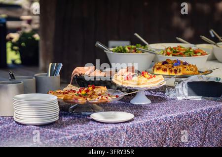 Un tavolo da buffet che mostra una varietà di torte alla frutta e pasticcini fatti in casa decorati con bacche fresche e fiori commestibili. Foto Stock