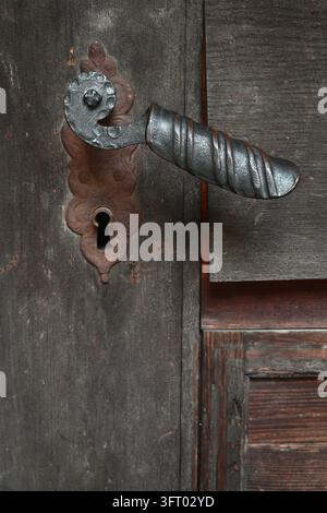 Primo piano di una maniglia vintage in ferro battuto e di una piastra della serratura arrugginita su una vecchia porta di legno stagionata. Foto Stock