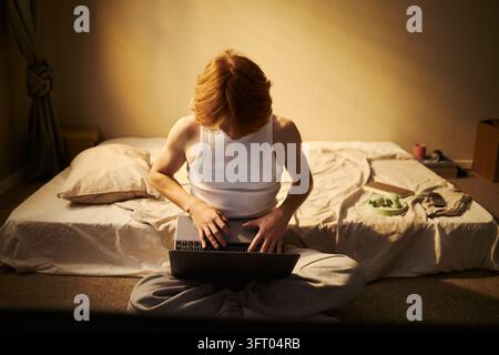 Uomo che lavora su un laptop seduto sul pavimento in un appartamento Foto Stock