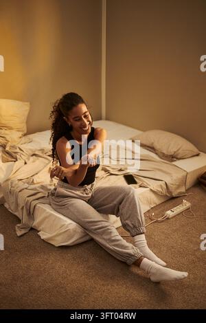 Donna biracial felice che allunga le braccia mentre si rilassa in camera da letto Foto Stock