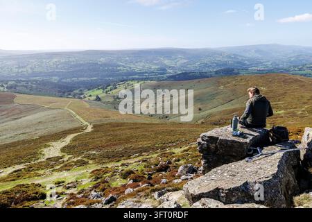 Uomo con una borraccia termica seduto sulla cima del monte Sugar Loaf, Abergavenny, Galles, Regno Unito Foto Stock