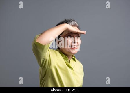 Donna matura espressiva che tiene la mano sopra gli occhi guardando con curiosità verso il futuro Foto Stock