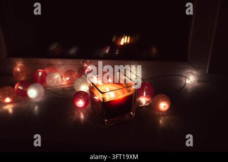 Candela rossa ardente con luci decorative festive in un ambiente accogliente e scuro Foto Stock