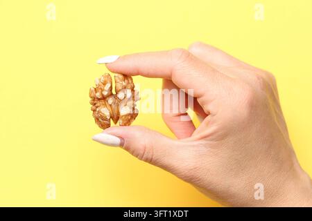 Donna che tiene una mezza noce tra le dita su sfondo giallo. Concetto alimentare in primo piano per spuntini sani, grassi naturali e nutrizione vegetale Foto Stock