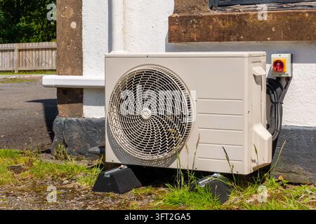 Unità compatta di pompa di calore esterna appoggiata su cuscinetti antivibrazione accanto a un muro intonacato, con interruttore di isolamento elettrico, cavi raggruppati e condensa Foto Stock