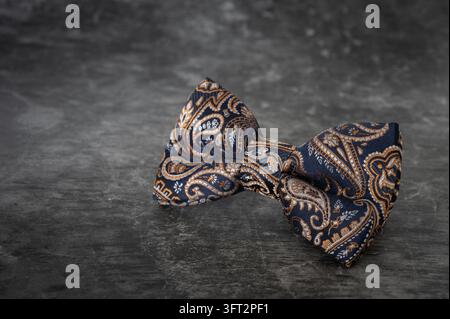 Un'elegante cravatta da uomo di lusso in seta blu scuro premium con un intricato motivo paisley in bronzo, oro e rame, esposta su un grigio scuro Foto Stock