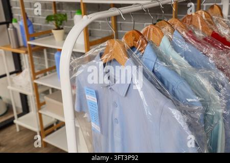 Servizio di lavaggio a secco e cura dei capi, camicie appena lavate su appendiabiti avvolte in coperture di plastica all'interno di una lavanderia professionale Foto Stock