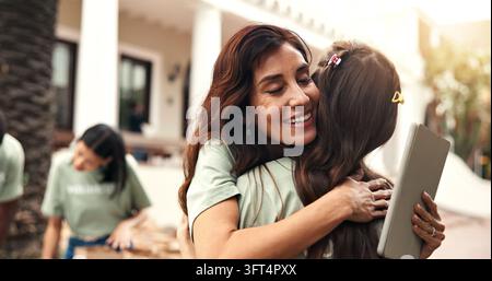 Sorriso, persone e abbraccio all'aperto per il volontariato, gratitudine e grazie per il servizio alla comunità. Donne felici e abbraccio con tablet per l'apprezzamento Foto Stock