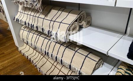 Tappeti in tessuto beige arrotolati con motivi a scacchi blu e marroni e bordi sfrangiati esposti su scaffali in un negozio di arredamento Foto Stock