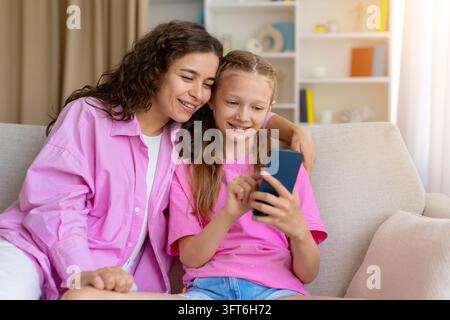 Madre e figlia felici che guardano insieme uno smartphone sedute sul divano Foto Stock