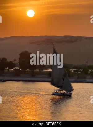 Osservare il tramonto sul Nilo ad Assuan in Egitto. Diverse barche a vela attraversano il fiume trasportando turisti e gente del posto Foto Stock