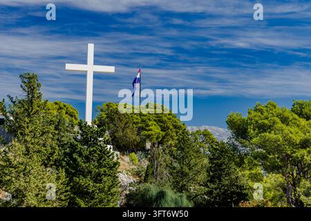 Una croce bianca alta sul colle di Marjan a Spalato, in Croazia, contro un cielo blu. Il simbolo religioso è un punto di riferimento noto sulla collina che si affaccia su t Foto Stock