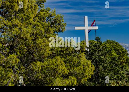 Una croce bianca alta sul colle di Marjan a Spalato, in Croazia, contro un cielo blu. Il simbolo religioso è un punto di riferimento noto sulla collina che si affaccia su t Foto Stock