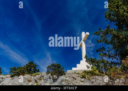 Una croce bianca alta sul colle di Marjan a Spalato, in Croazia, contro un cielo blu. Il simbolo religioso è un punto di riferimento noto sulla collina che si affaccia su t Foto Stock