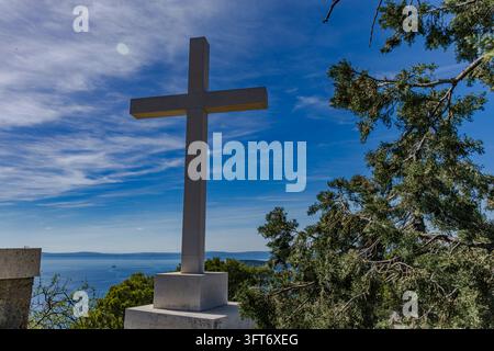 Una croce bianca alta sul colle di Marjan a Spalato, in Croazia, contro un cielo blu. Il simbolo religioso è un punto di riferimento noto sulla collina che si affaccia su t Foto Stock