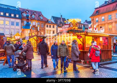 Bamberg, Germania – 28 novembre 2025. Persone che passeggiano attraverso un mercato tradizionale invernale illuminato al crepuscolo. Foto Stock
