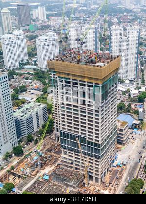 Vista aerea di un grattacielo in costruzione con più gru in cima e edifici alti urbani circostanti a Jakarta, Indonesia. Foto Stock