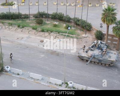 Un carro armato M2A3 Bradley posizionato vicino a un cartello "Benvenuto" e a palme fuori dall'hotel Ishtar Sheraton a Baghdad, Iraq, nel marzo 2004. Foto Stock