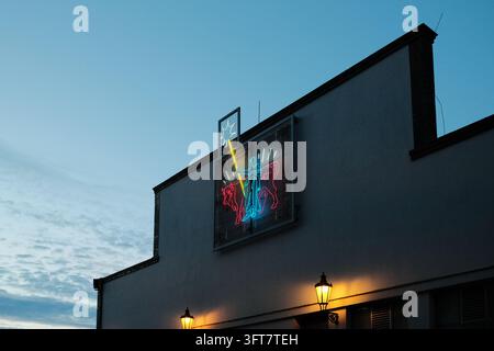 Praga, Repubblica Ceca - 13 ottobre 2026: Vista ad angolazione bassa di un'opera d'arte al neon in rosso, blu, giallo e bianco su un muro con una camino, due lampade accese a Foto Stock