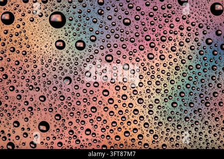 Gocce d'acqua che formano un motivo testurizzato su una superficie colorata, creando uno sfondo astratto vibrante con riflessi iridescenti Foto Stock