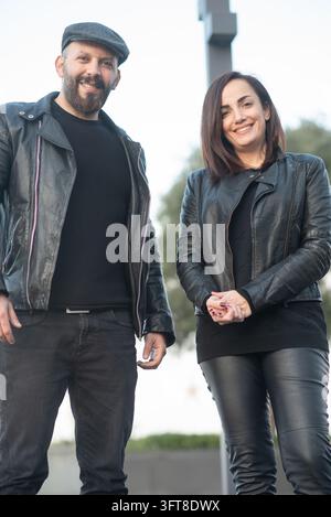 Un uomo e una donna sorridenti che indossano giacche di pelle nera stanno insieme all'aperto in un contesto urbano. Foto Stock