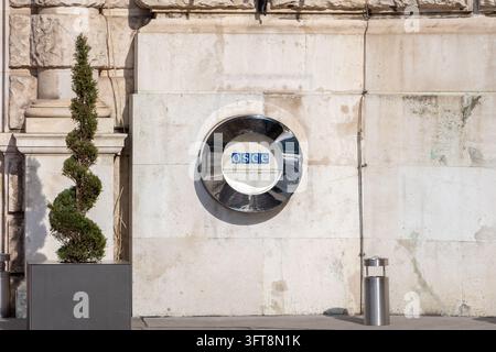 VIENA, AUSTRIA, 26 febbraio 2026: Il logo dell'OSCE è montato su un muro di pietra consumato accanto a una pianta topiaria scolpita in vaso. Foto Stock