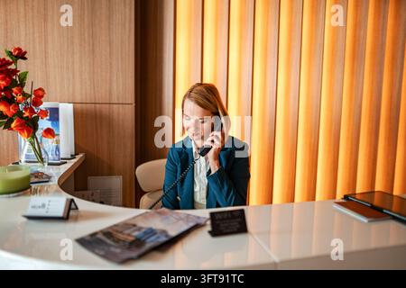 Addetta alla reception che risponde a una chiamata telefonica alla reception dell'hotel Foto Stock