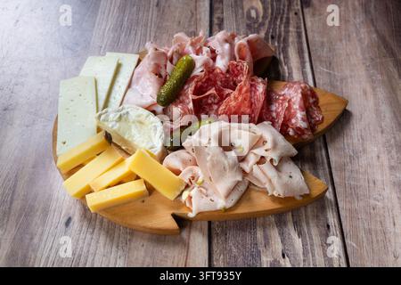 Vari salumi affettati, salami e formaggi con sottaceti disposti su un vassoio di servizio in legno. Foto Stock