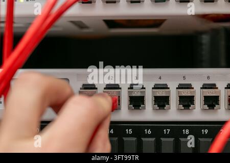 Primo piano di una mano che inserisce un cavo patch Ethernet in una porta di rete su uno switch o pannello patch all'interno di uno rack server. Foto Stock