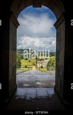 CHATSWORTH, REGNO UNITO - 15 LUGLIO 2023: Un arco in pietra della Cascade House incornicia l'acqua che scende lungo la cascata verso Chatsworth House, con Foto Stock