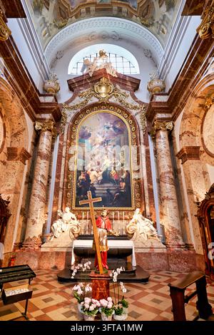 Altare laterale barocco con un paliotto dorato, colonne di marmo e un santo che tiene una croce all'interno della Chiesa di San Carlo a Vienna, Austria Foto Stock