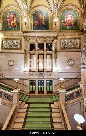 Interno della Staatsoper di Vienna sulla Ringstraße con scalini in marmo, tappeto verde, lunette dipinte e rilievi di balletto e opera Foto Stock